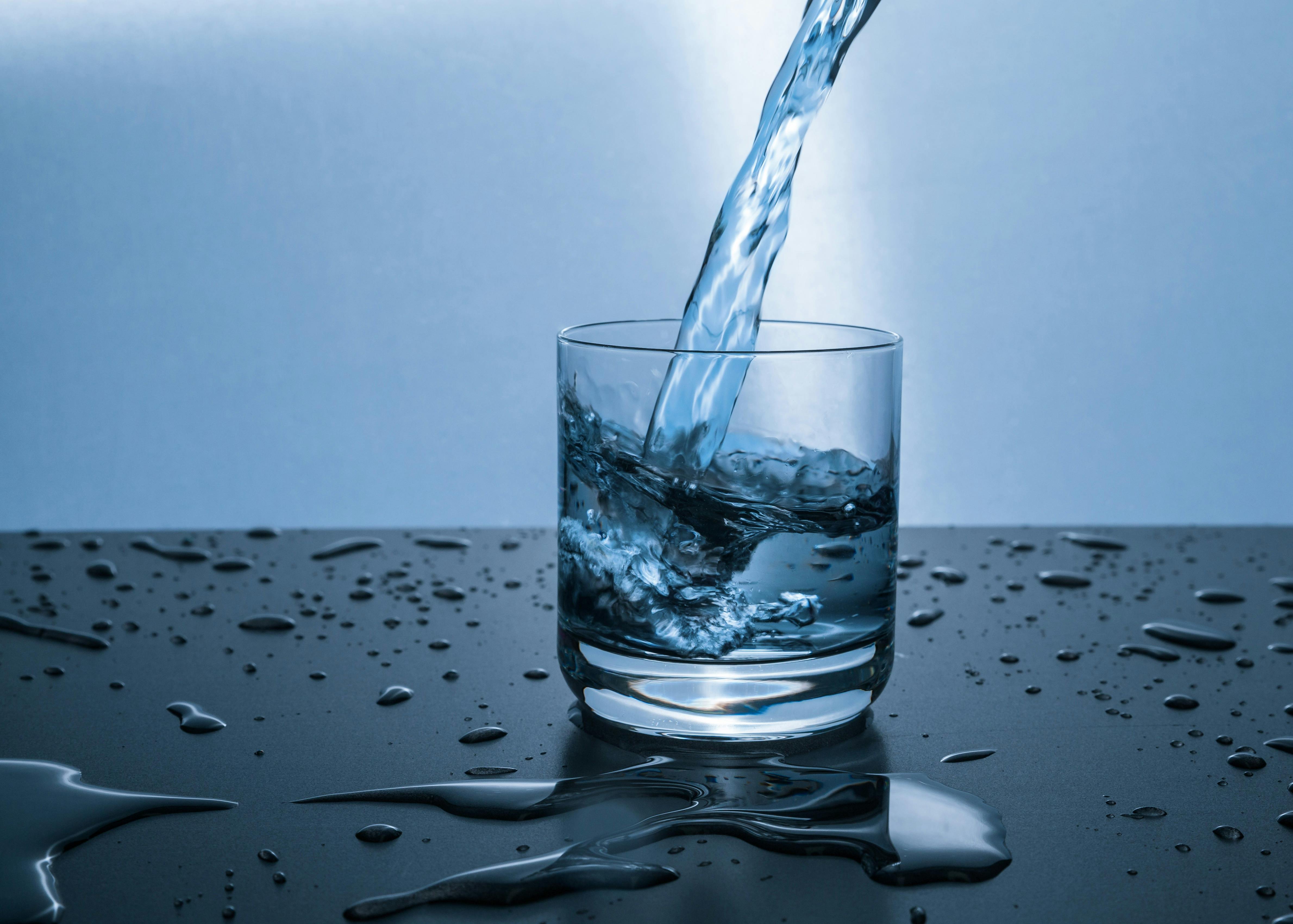 A refreshing glass of water with ice and a lemon slice, on a clean, bright background.